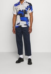 Kortärmad skjorta med blå, svart och beige abstrakta mönster. Bärs med marinblå byxor och svarta skor. Slät tyg och avslappnad passform.