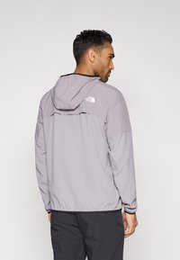 Ανοιχτό γκρι μπουφάν με κουκούλα, ελαστικές μανσέτες και τελείωμα, με μαύρο λογότυπο στην πλάτη. Λείο ύφασμα και άνετη εφαρμογή.