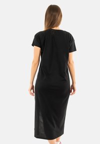 Robe noire, longueur genoux, avec des manches courtes, fabriquée en tissu doux. Coupe droite avec des fentes latérales pour faciliter le mouvement. Sans motifs ni accents visibles.