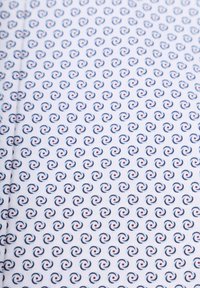 Witte stof met een herhalend patroon van kleine blauwe en rode krullen, wat een gelijkmatige textuur over het oppervlak creëert.