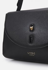 Czarna torebka skórzana o teksturowanej powierzchni z zaokrągloną klapą, złotym zapięciem oraz wytłoczonym logo "LYDC LONDON" z przodu.