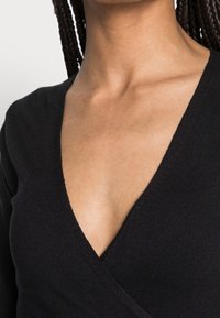 Pull col en V noir avec texture côtelée et design à enroulement, mettant en valeur une silhouette ajustée et un décolleté lisse.