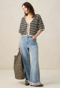 Pull cropped à rayures noires et blanches avec un col en V et un lien de fermeture, associé à un jean large bleu et un sac fourre-tout en imprimé léopard.