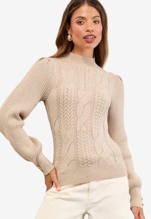 Beige Kabelstrickpullover mit hohem Kragen, gerippten Ärmeln und goldenen Knopfakzenten an den Bündchen. Weiche Textur und taillierte Passform.
