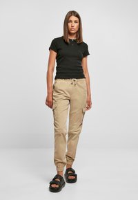 Svart tettsittende t-skjorte med ribbet tekstur, kombinert med beige cargo-bukser med sidelommer og elastiske mansjetter, båret med svarte sandaler.