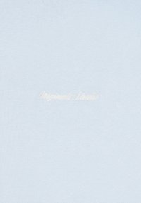 Jasnoniebieska tkanina z subtelnym białym haftowanym napisem "Originals Studio" umieszczonym na środku powierzchni.