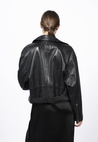 Czarna skórzana kurtka o skróconym kroju, szerokim kołnierzu i widocznym szwie. Posiada zamek błyskawiczny przy mankietach oraz naszywkę z logo na plecach.