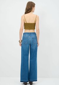 Olijfgroen crop top met gerimpelde textuur en dunne bandjes, gecombineerd met lichtblauwe wijdlopende denim jeans, voorzien van achterzakken en een rafelrand.