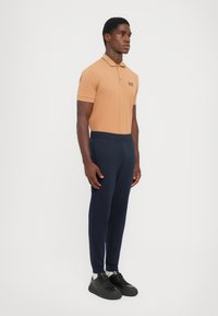 Tan polo shirt with collar and logo, paired with navy joggers featuring elastic waist. Black sneakers complete the outfit.