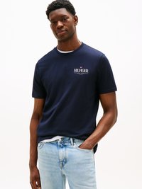 Navy blue cotton T-shirt with a crew neck, featuring a white logo chest print and short sleeves, paired with light blue jeans.