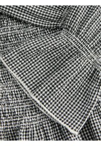 Tissu à petits carreaux noir et blanc avec coutures visibles et sections superposées pliées.