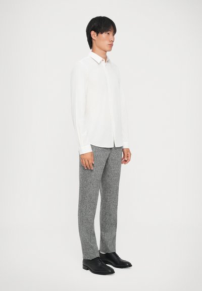 Camicia bianca con colletto, pantaloni grigi a trama e scarpe nere. La camicia presenta un colletto con bottoni, mentre i pantaloni hanno una vestibilità su misura.