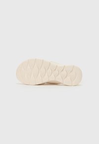 Lys beige sneaker såle med en teksturert gummioverflate, som har et ovalt mønster for grep og en glatt, avrundet bakkant.