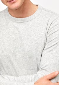 Grau langärmliges Shirt aus weichem, strukturiertem Stoff mit Rundhalsausschnitt. Bietet eine lässige Passform und sichtbare Nähte entlang der Nähte.