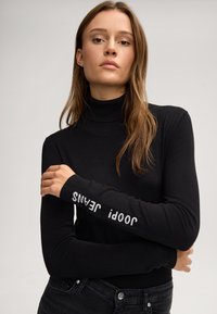 Czarny sweter z golfem i długimi rękawami, na lewym rękawie z białym napisem "jeans". Wykonany z gładkiego, lekkiego materiału.