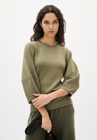 Olivengrüner, langärmeliger Sweatshirt mit Rundhalsausschnitt, strukturiertem Stoff und weit geschnittenen Ballonärmeln. Kombiniert mit passenden Hosen.