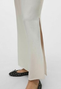 Robe midi beige et crème avec une fente latérale, fabriquée en tissu doux. Portée avec des ballerines noires à motif avec un accent en nœud.