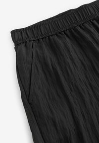 Pantaloni neri in tessuto intrecciato con vita elasticizzata, caratterizzati da una texture plissettata e tasche laterali per una maggiore funzionalità.