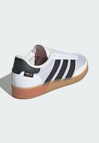 White sneaker featuring black stripes, mesh upper, rubber outsole with a gum color, and reinforced heel with a fabric tag marked "CORDURA."