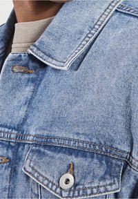 Jasnoniebieska kurtka dżinsowa z klasycznym kołnierzem, przednimi kieszeniami i srebrnymi detalami. Posiada wstawkę szwów i lekko wyblakłą teksturę.
