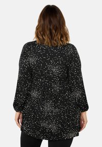 Black tunic top featuring white speckles, long sleeves, and a gathered waistline. Soft fabric with a relaxed fit and rounded hem.
