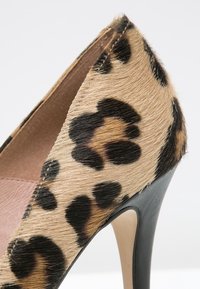 Chaussure à talons hauts avec texture en fourrure imprimé léopard et talon aiguille noir sur fond blanc.