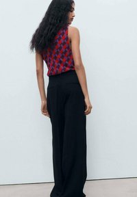 Sleeveless top featuring a red and purple diamond pattern, paired with black wide-leg trousers. Smooth fabric with a relaxed fit.