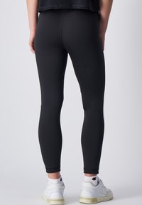 Leggings negros hechos de material elástico, con una textura suave y un diseño ajustado, con una pierna ajustada y un acabado limpio en el tobillo.