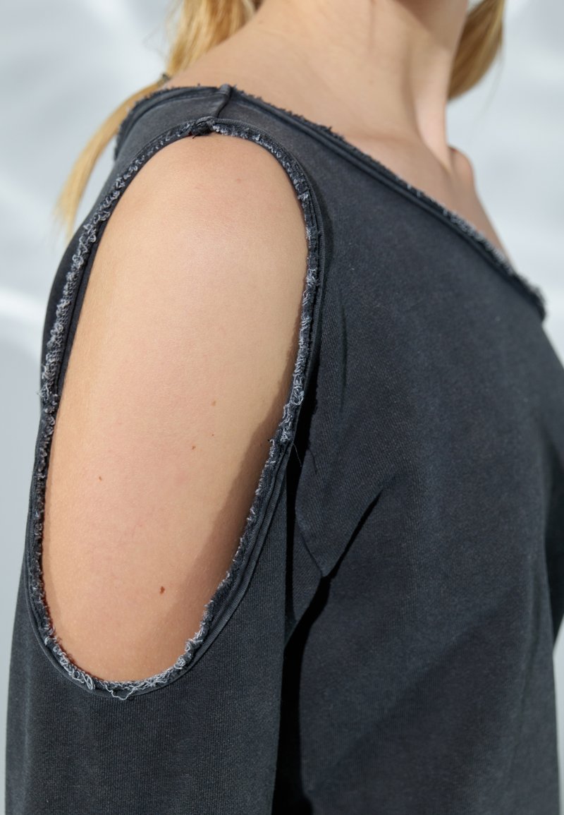 Maglietta nera a maniche lunghe con spalle a taglio, orli sfrangiati e texture morbida, caratterizzata da una vestibilità rilassata e scollo rotondo.