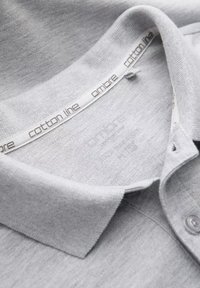 Camisa polo de algodón gris con una tela texturizada, cuello doblado y una etiqueta con la marca "cotton line" visible en el cuello.