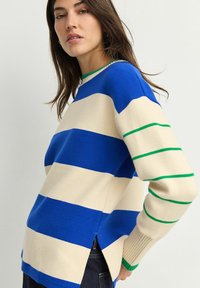 Blauw en crème gestreepte gebreide trui met groene accenten op de halslijn en manchetten, met een inkeping aan de zijkant en ribgebreide manchetten.