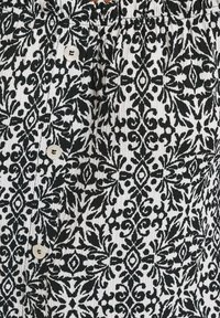 Svart och vitt mönstrat tyg med intrikata blommönster. Har små, runda knappar. Texturerad yta med plisserade detaljer.