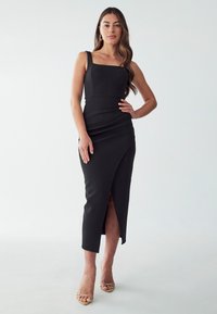 Black fitted midi dress with a square neckline and thick straps, featuring a side slit and ruched detailing for texture.