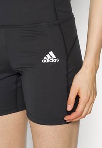Černé sportovní šortky z elastické látky. Mají prošité švy a bílý logo Adidas na levém stehně.