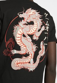 Černé tričko s bílým a korálovým grafikou draka, se složitými šupinami a akcenty, a japonským textem na zadní straně.