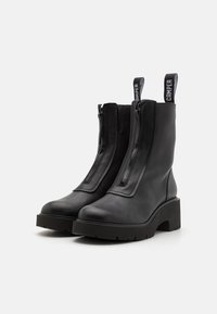 Black leather ankle boots with a smooth texture, featuring a thick platform sole, front zipper, and a pull tab marked "Camper."