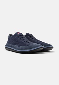 Navy blue sneakers with a mesh upper and suede accents, featuring a rounded toe and flat rubber sole. Laces are dark blue with red branding detail.