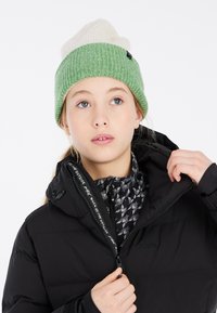 Beanie lavorato a maglia con una sezione inferiore verde e una superiore bianca, caratterizzata da una finitura testurizzata. Giacca invernale nera con uno strato interno grafico.
