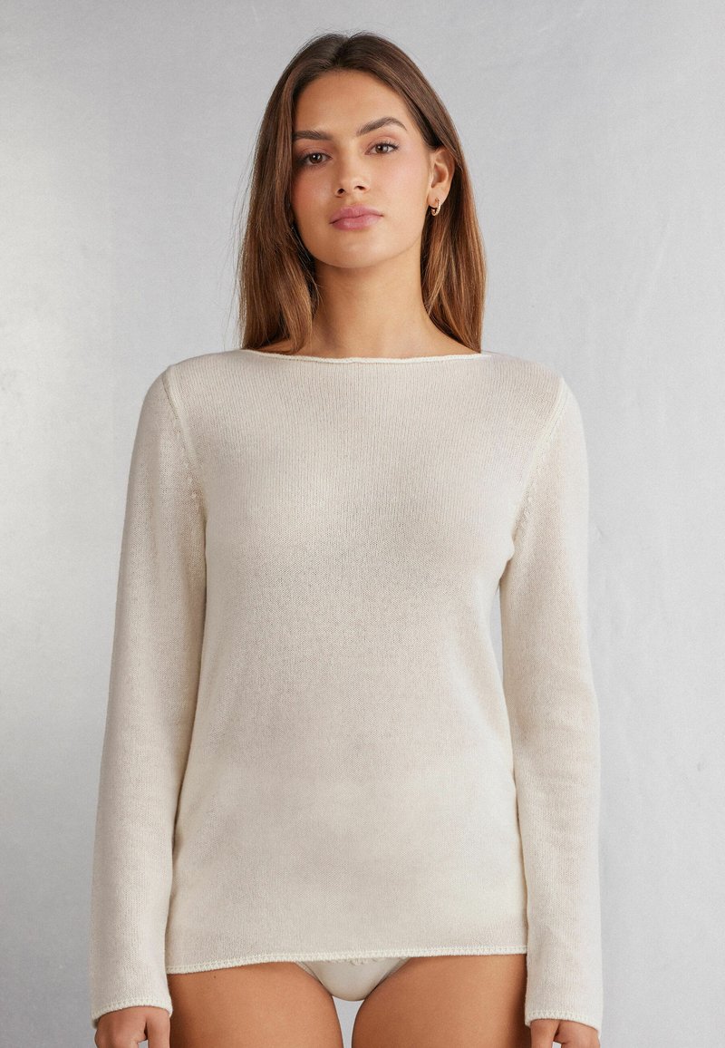 Pull long beige clair à manches longues ; texture douce et tricotée ; décolleté bateau ; fini avec une bordure tricotée contrastante au niveau de l'ourlet et des poignets.