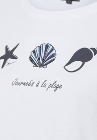 White cotton t-shirt featuring a starfish, a blue shell, and a black seashell illustration, with the text "Journées à la plage" below.