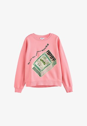 Pink sweatshirt med en grafik af en grøn matcha-tepakke og teksten "We are the perfect matcha" hældt over den.