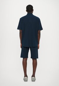 Marineblaues Kurzarmhemd mit geradem Schnitt, kombiniert mit passenden Shorts. Der Stoff wirkt leicht und glatt, mit einem schlichten Design.