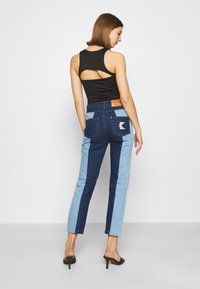 Jeans de denim con un diseño a bloques de color en azul oscuro y claro, con un logo en el bolsillo trasero y un parche de cuero marrón en la cintura.