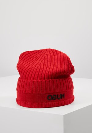 Bonnet en tricot côtelé rouge avec revers plié et broderie du logo noir "HUGO" posé sur une surface blanche.