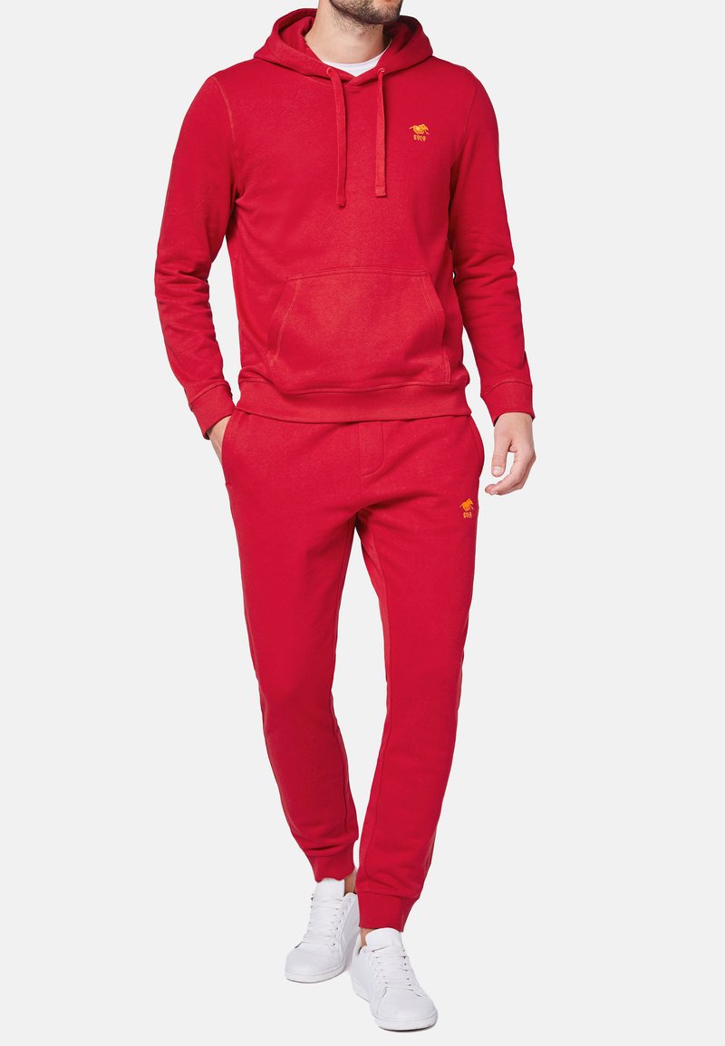 Felpa rossa in cotone con tasca frontale e cappuccio con cordino, abbinata a pantaloni jogger coordinati. Presenta un piccolo logo giallo sul petto.