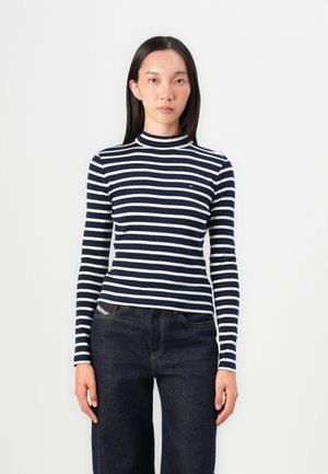 Marinblå och vitrandig polotröja med långa ärmar, tillverkad av ett mjukt tyg. Bärs med mörkblå vida jeans som har en framlomma.