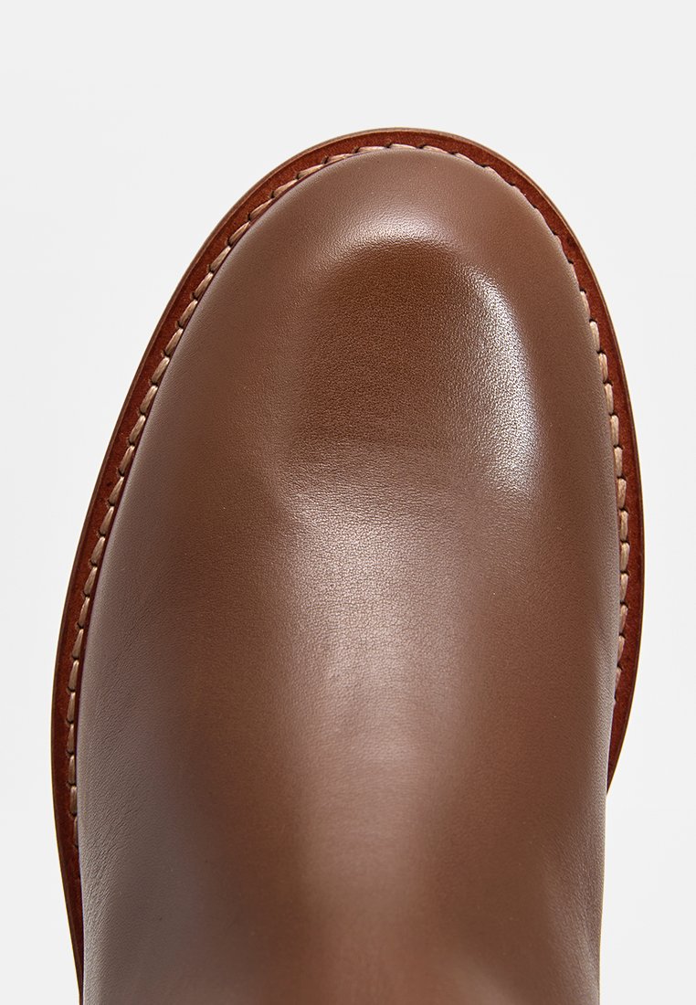 Brauner Lederknöchelboot mit glatter Oberfläche, rundem Zehenbereich und kontrastierender Naht entlang der Kante. Einfaches und robustes Design.
