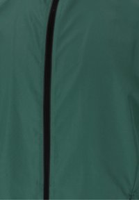 Tissu de veste verte avec une fermeture éclair noire centrée, courant verticalement, montrant une texture lisse et des détails de couture légers.