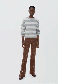 Grå och vit randig stickad tröja med lång ärm, kombinerad med bruna utsvängda kordflossbyxor med metalliska prickdetaljer.