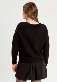 Black knitted sweater with a relaxed fit, wide neckline, and long sleeves, paired with black shorts, showcasing a soft, textured finish.